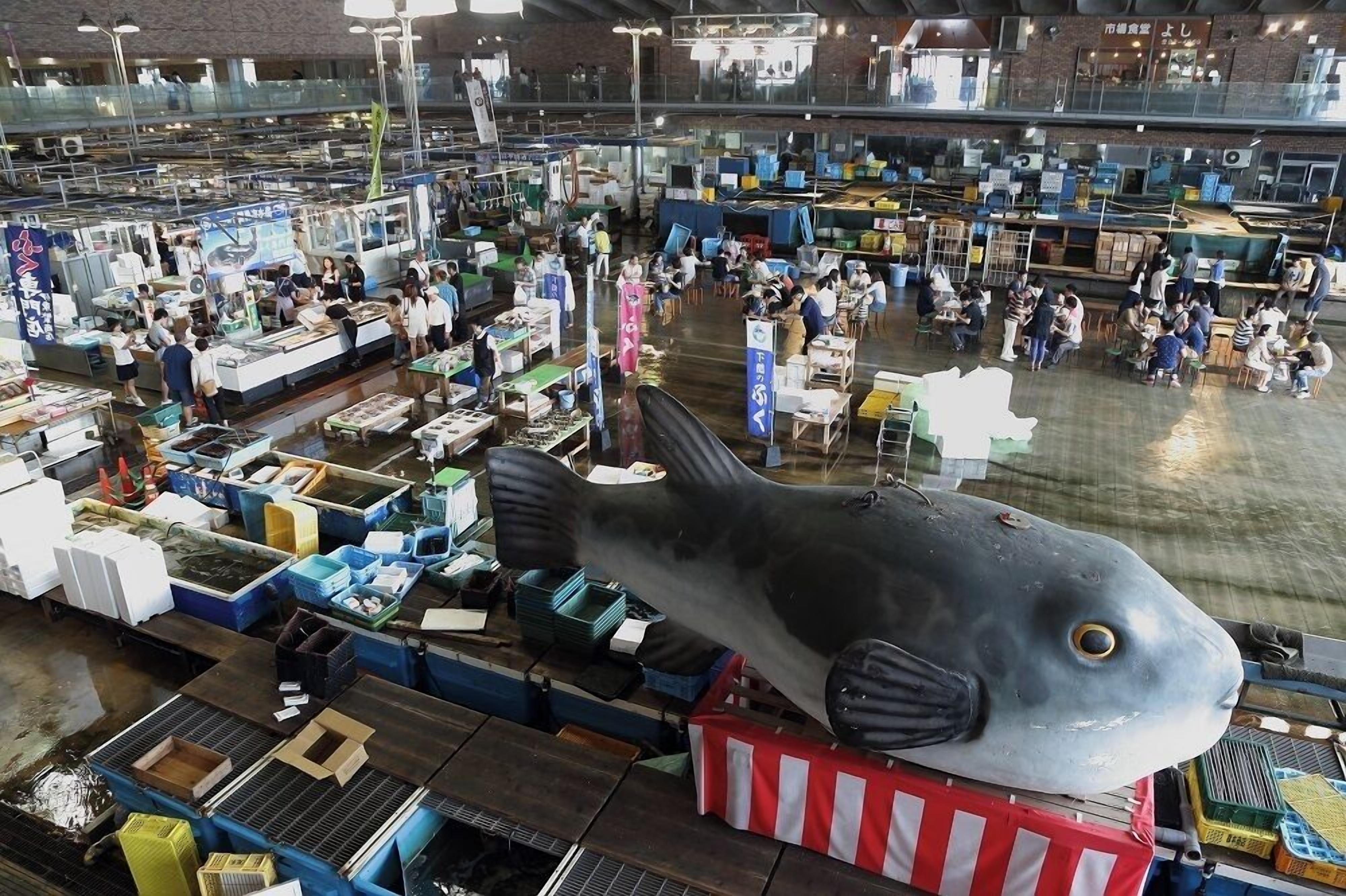 Un mercat interior espaiós amb nombrosos puestos i una escultura de peix destacada.