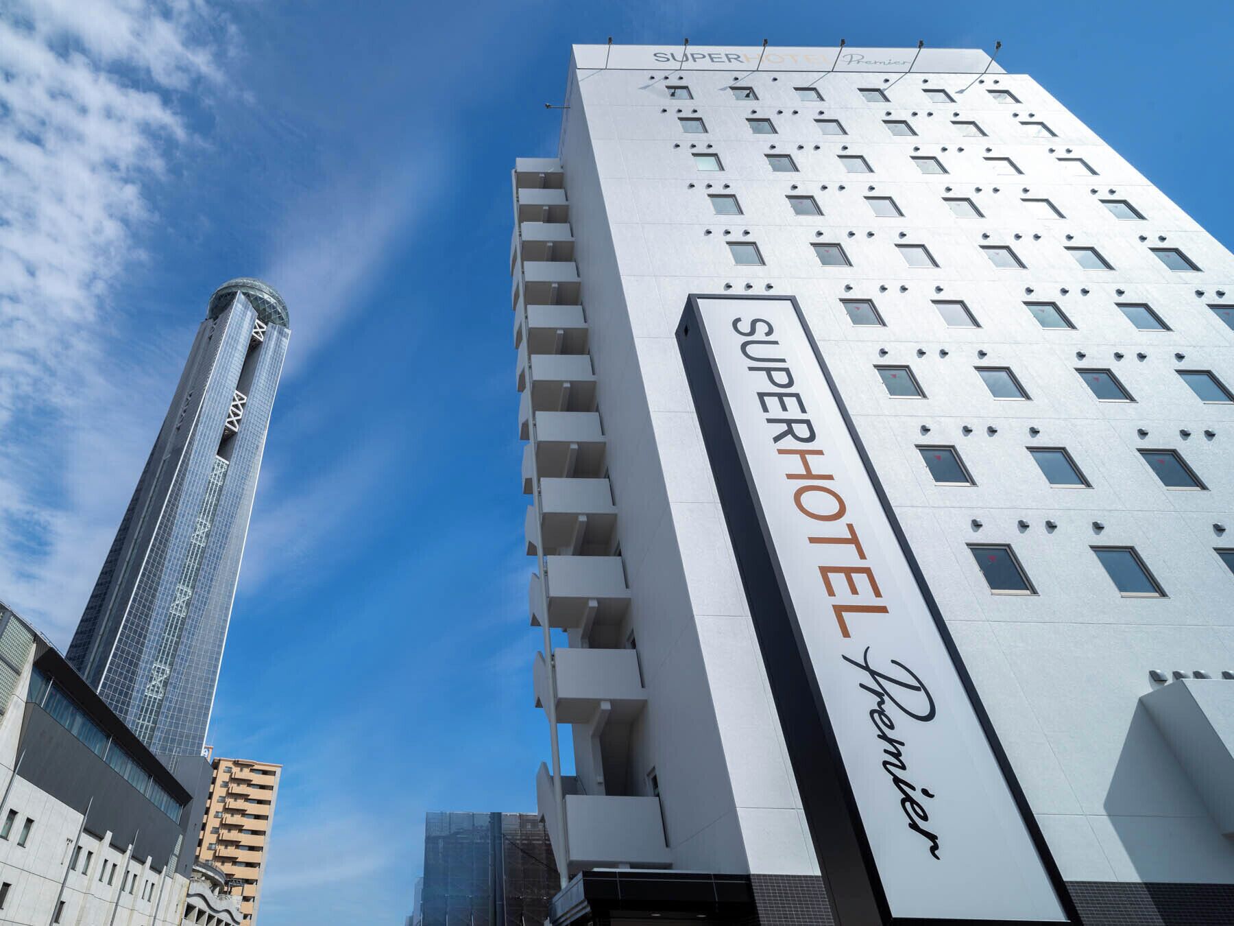 Edificio del SuperHotel Premier con diseño moderno, destacando un letrero y un cielo despejado al fondo.