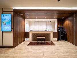 Un vestíbulo de hotel moderno con un mostrador de recepción, una pantalla digital que muestra información y un quiosco de autoservicio.