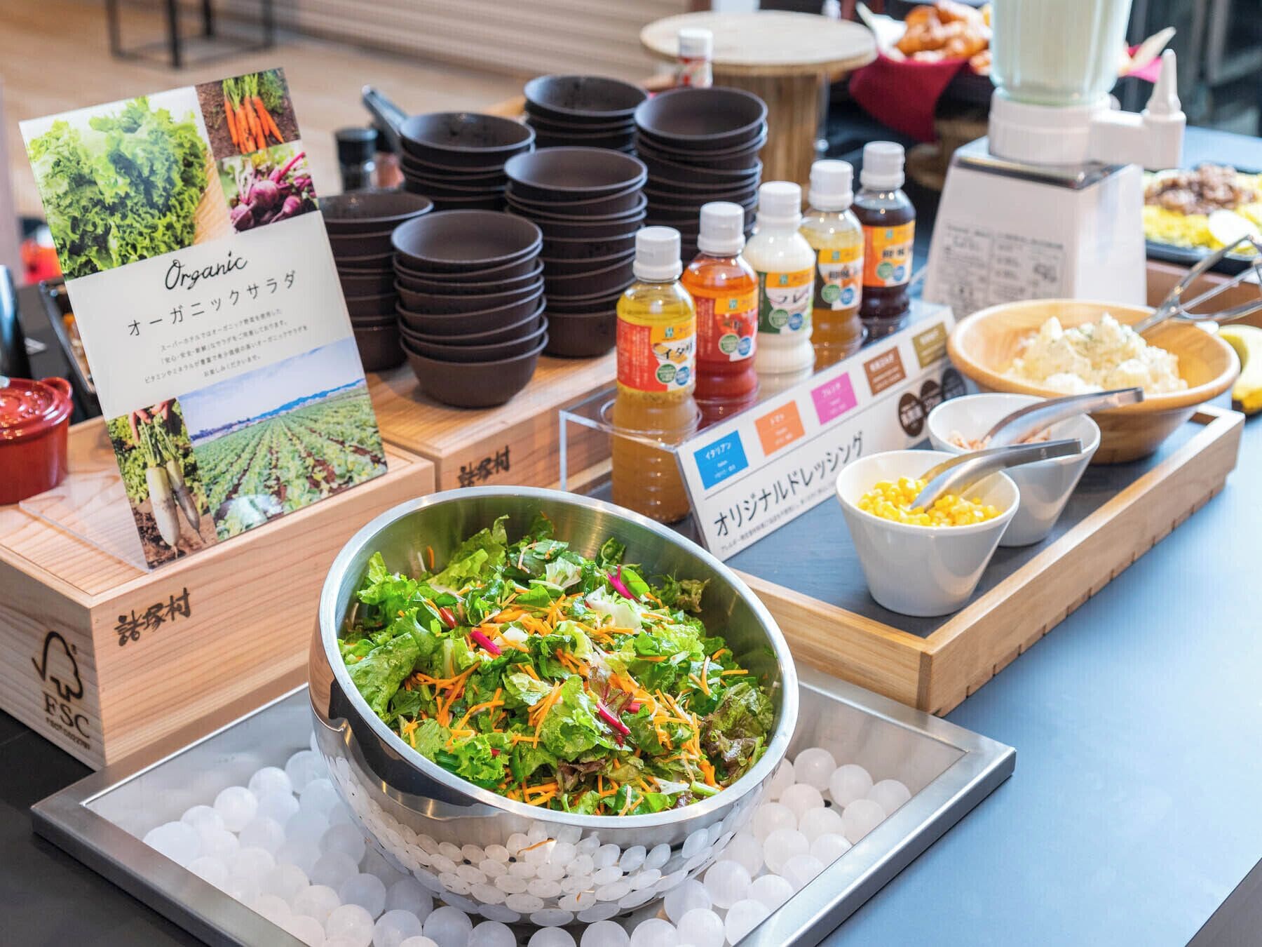 Uma mesa de buffet com uma saladeira, condimentos e pratos empilhados.