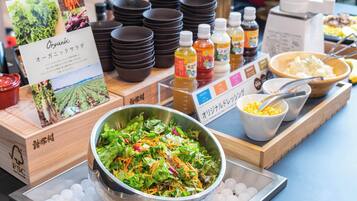 Uma mesa de buffet com uma saladeira, condimentos e pratos empilhados.