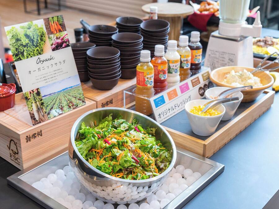 Uma mesa de buffet com uma saladeira, condimentos e pratos empilhados.