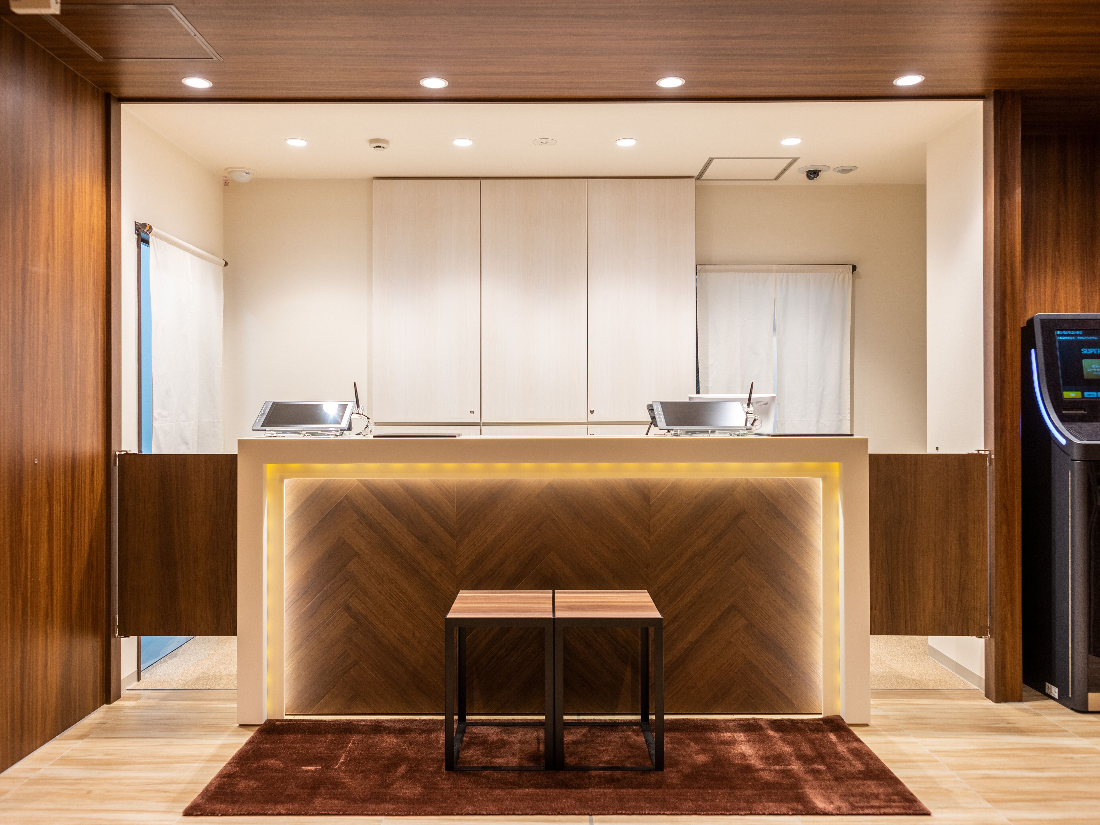 Un mostrador de recepción moderno con detalles de madera, una pequeña mesa al frente y un quiosco de autoservicio a la derecha.