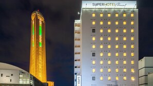 A SuperHotel Premier building with a modern design, featuring a prominent tower with illuminated windows and a flat facade with evenly spaced windows. - Super Hotel Premier Shimonoseki (Shimonoseki)