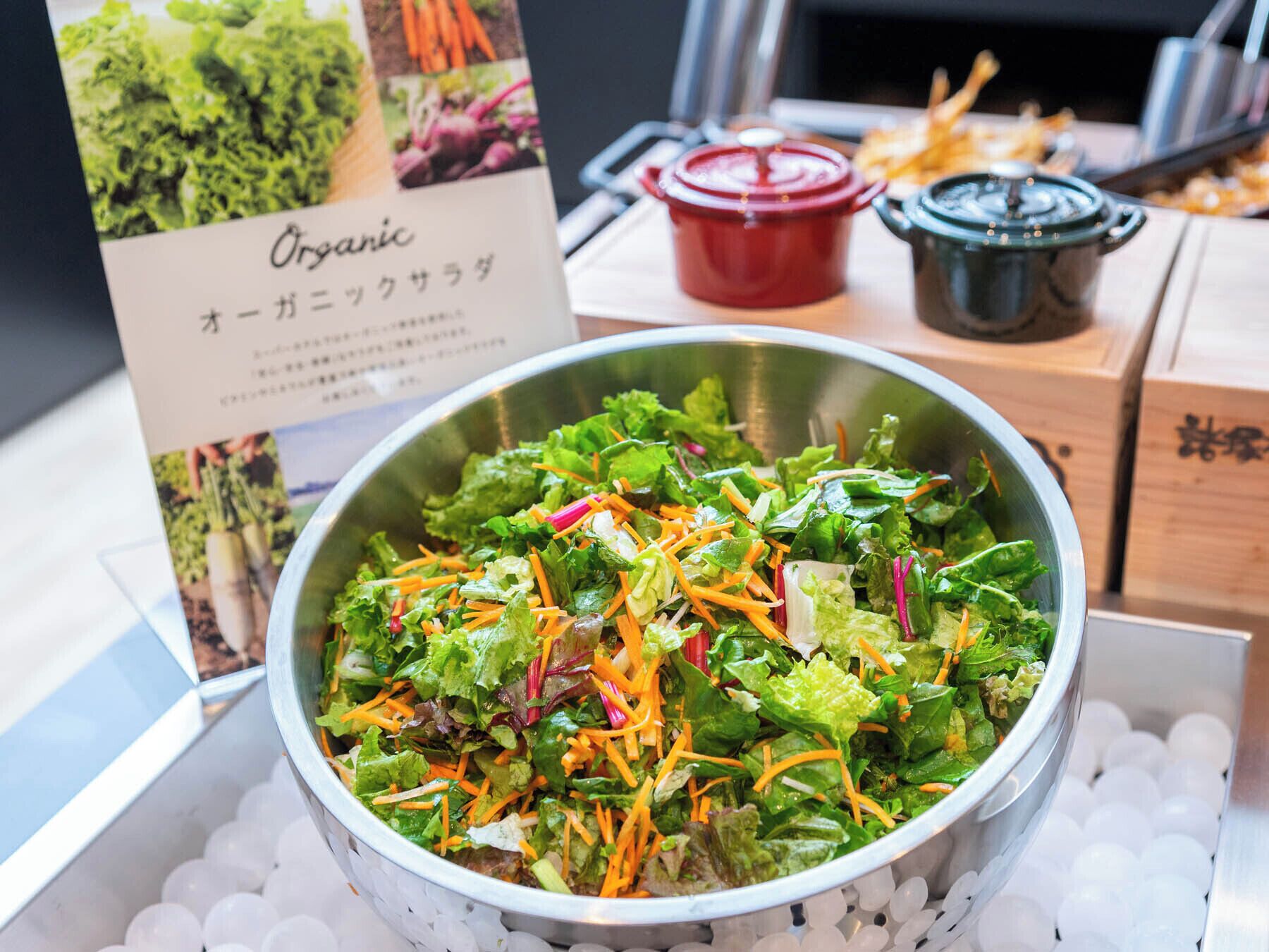A salad bowl with various greens and shredded carrots, placed on a bed of ice.