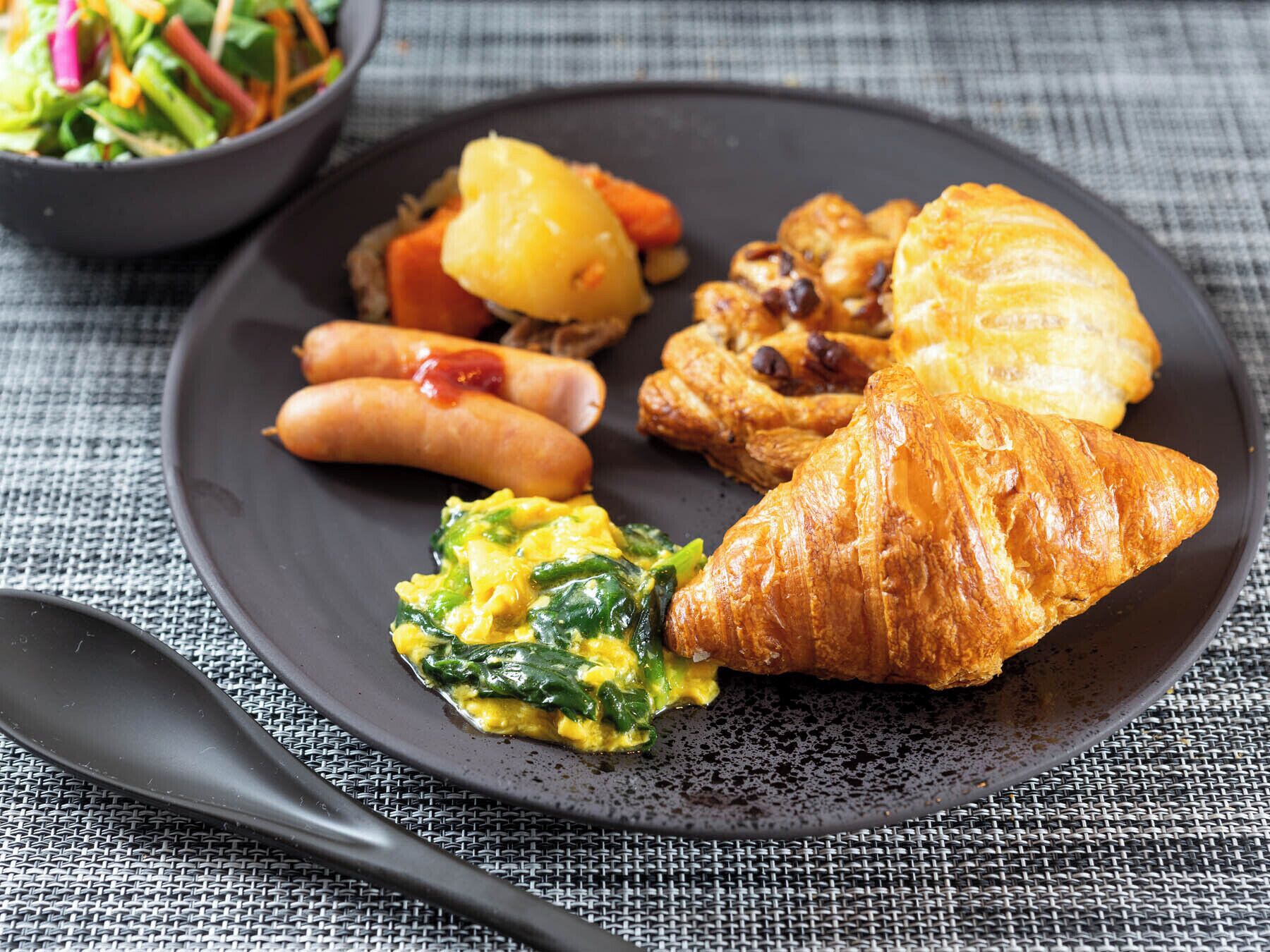 A plate with food items including sausages, a croissant, scrambled eggs, and a salad.
