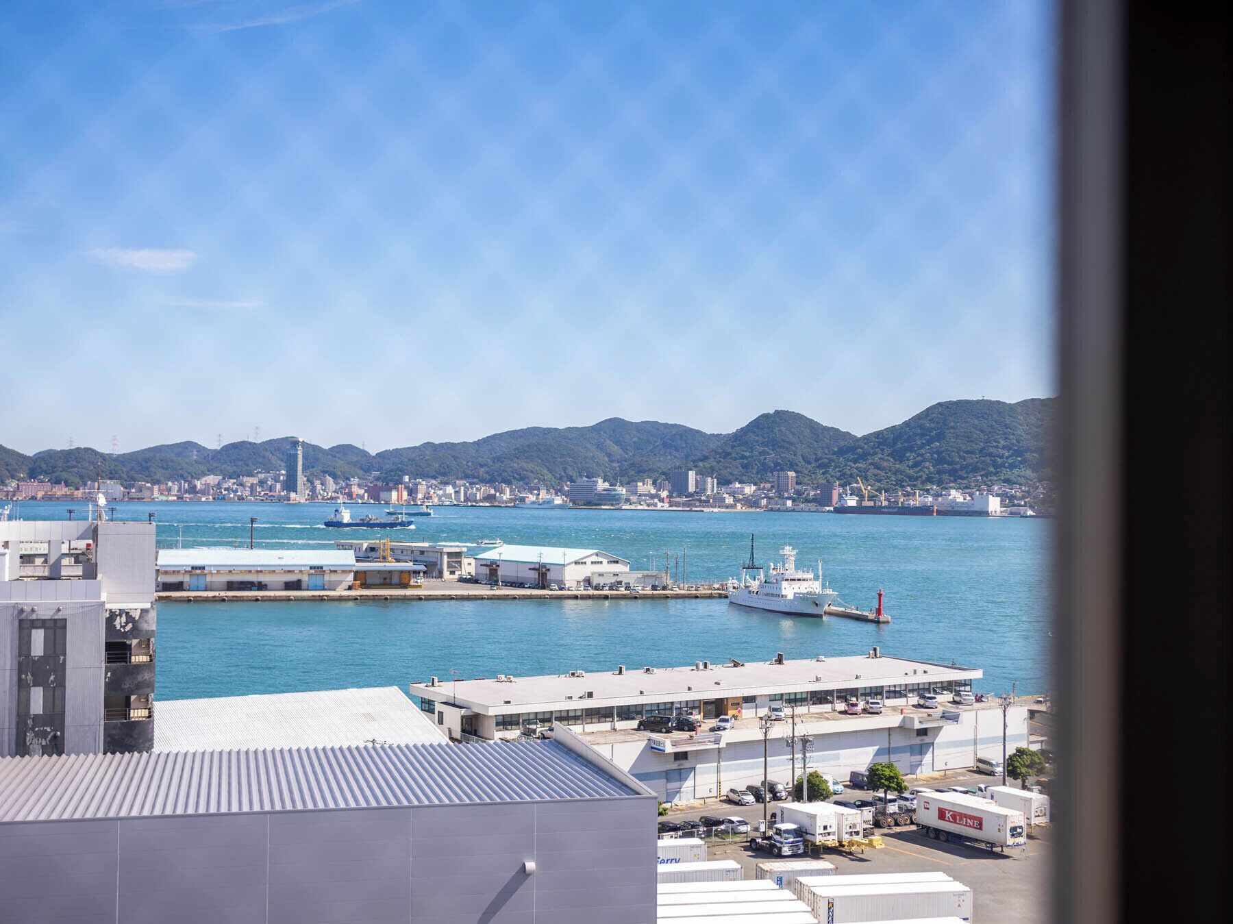 A coastal cityscape with a marina, buildings, and mountains in the background.