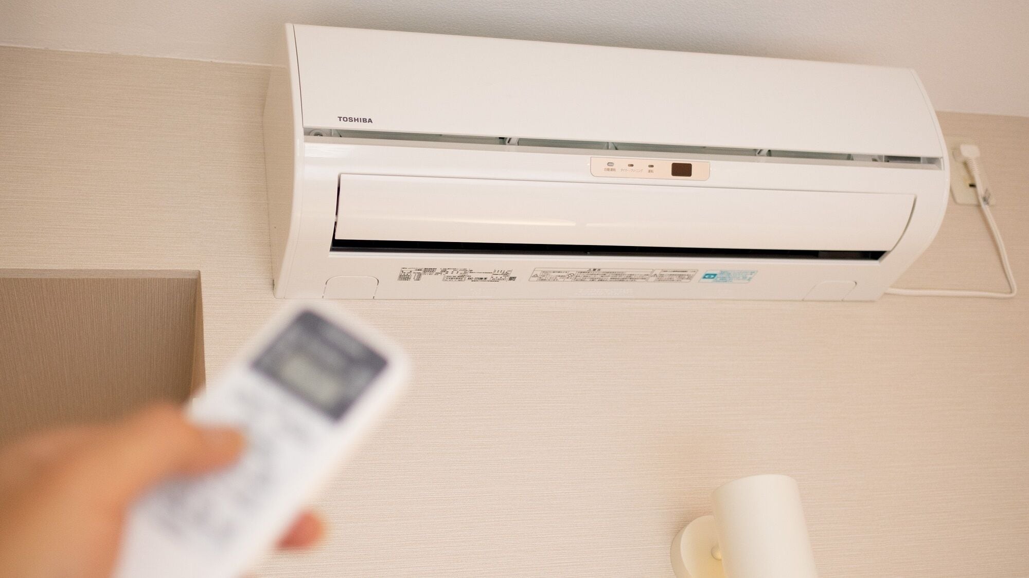 A white air conditioning unit mounted on a wall with a remote control in hand.