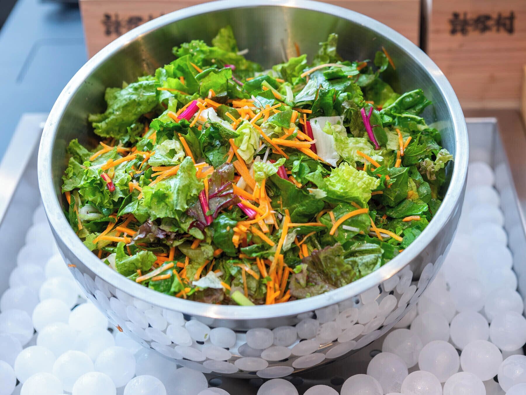 A metal bowl filled with a salad on ice, surrounded by white spherical ice cubes.