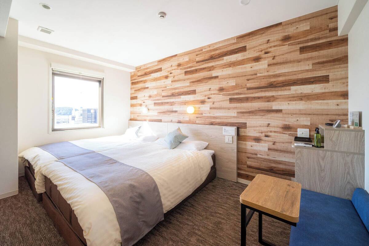 A hotel room with a bed, a small table, a desk, and a wooden wall.