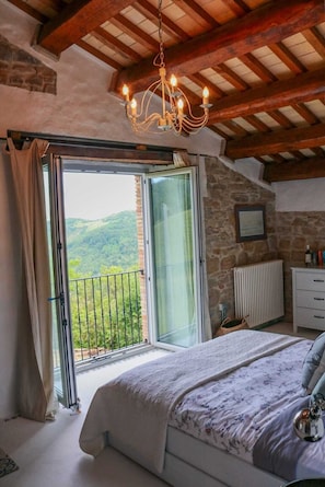 A bedroom with a large bed, a chandelier, a stone wall, and a view of the outdoors.