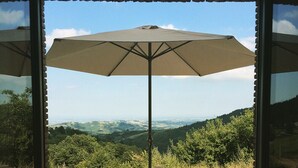 Une table avec un parasol, deux chaises et une vue sur la campagne, visible à travers une porte vitrée.