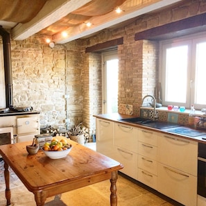 A kitchen with stone walls, a wooden table with fruit, and a window with a view.