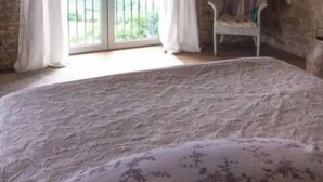 Une chambre avec un mur en pierre, un plafond en bois, un lit, une chaise et une vue sur l’extérieur, visible à travers une porte vitrée.