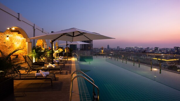 Una piscina infinita con vistas a la ciudad, sillones de descanso y un área de bar.