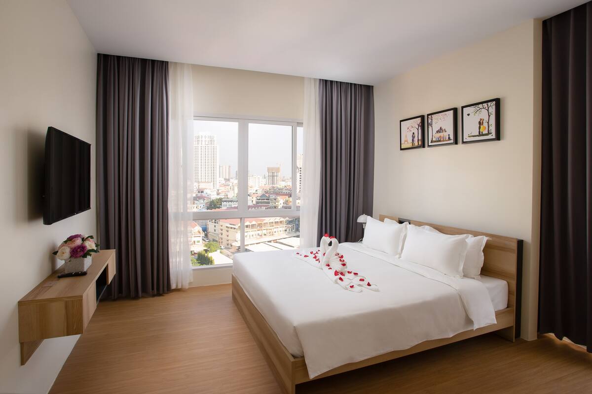 Habitación de hotel con una cama grande, un televisor en la pared y vistas a la ciudad.