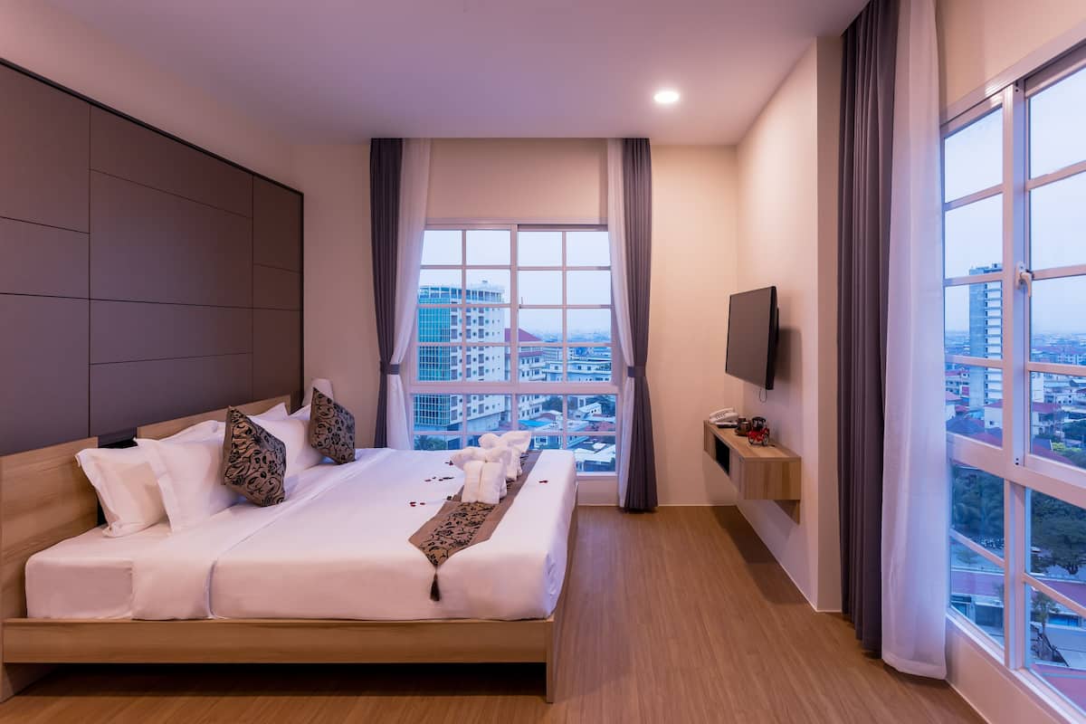 Una habitación de hotel moderna con una cama grande, un televisor en la pared y vistas a la ciudad a través de la ventana.