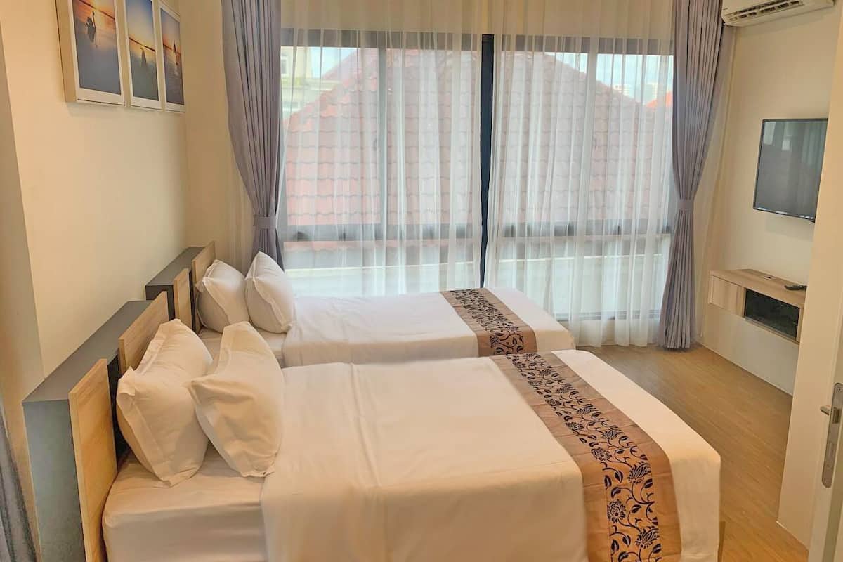 Habitación de hotel con dos camas, televisión y un gran ventanal con cortinas.