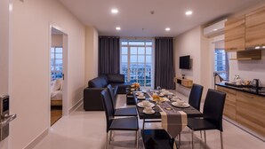 Un comedor moderno con una larga mesa dispuesta para cuatro personas, sillas negras y vistas a la ciudad a través de grandes ventanales.
