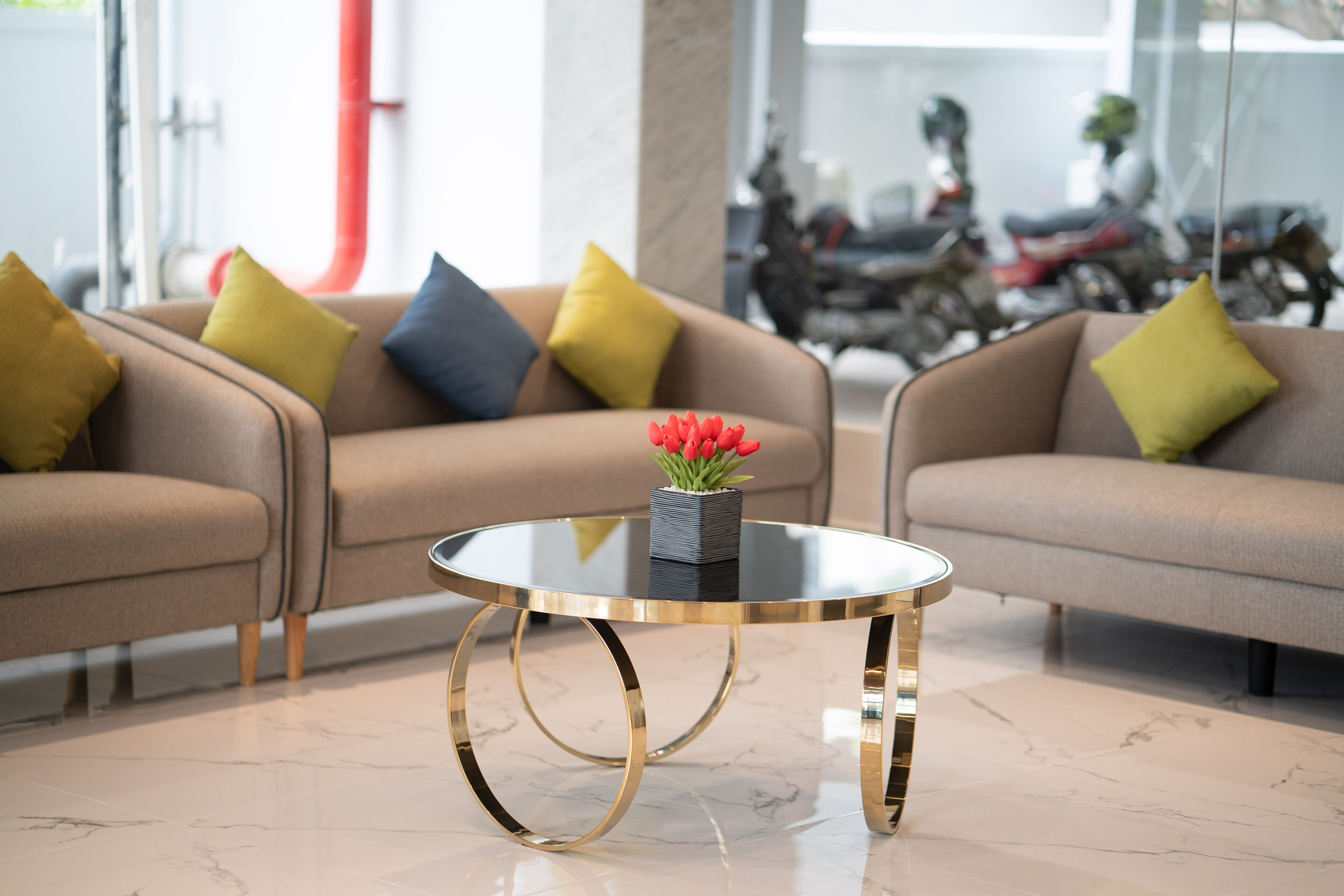 A modern living room with two sofas, a glass coffee table, and a vase with red flowers.