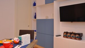 Una habitación con una mesa de comedor dispuesta con una taza roja, un plato blanco y una cuchara. Hay una silla, una pared azul y un estante con un jarrón azul.