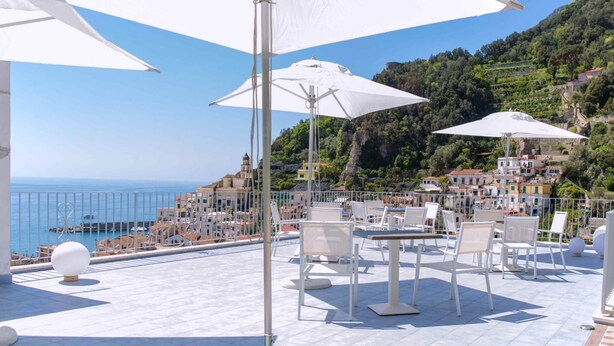 Terraza con mobiliario exterior y sombrillas con vistas a un pueblo costero.