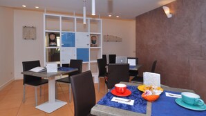 Un comedor con mesas y sillas, algunas computadoras portátiles y algunas personas al fondo.