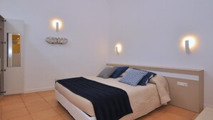 Un dormitorio ordenado con cama, lámparas de noche y una lámpara fijada a la pared.