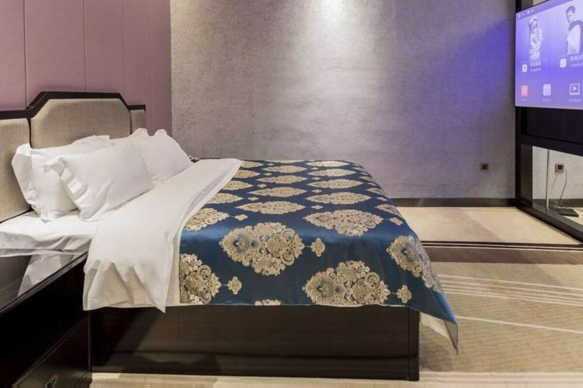 Et hotelværelse med en seng, et fjernsyn og en vægmonteret lampe.