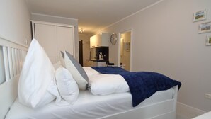 A bedroom with a bed, a white wardrobe, a small kitchenette, and a bathroom visible through an open door.