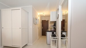 A compact room with a wardrobe, a small kitchenette, and a white chair.