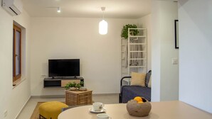 Un salon moderne avec un téléviseur à écran plat, un canapé, une table à manger avec des tasses et un bol, et une petite plante.