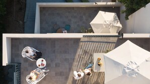 Vue aérienne d’une terrasse sur le toit, avec plusieurs tables et chaises, des parasols et un espace salon.