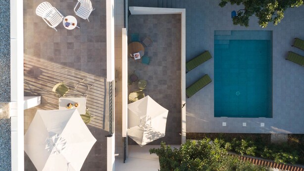 Vue aérienne d’un espace piscine aménagé sur un toit, avec des chaises longues, des parasols et une piscine.