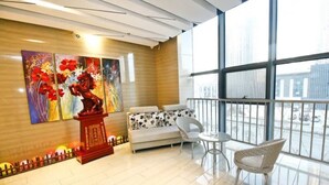 A modern hotel room with a large window, a sofa, a chair, and a decorative red stand with floral artwork. - Urba Hotel · Xi'an North Railway Station (Xi'an)