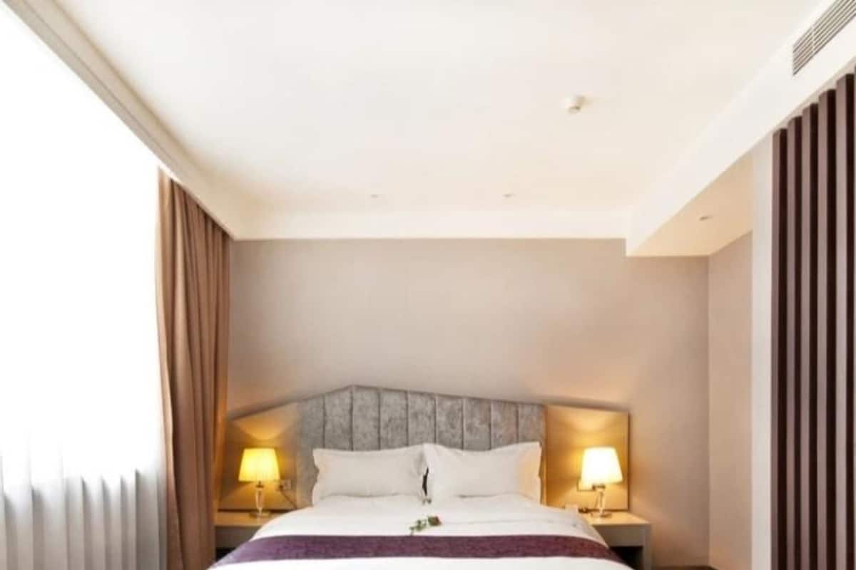 A hotel room with a large bed, two bedside tables with lamps, a headboard, and a window with curtains.