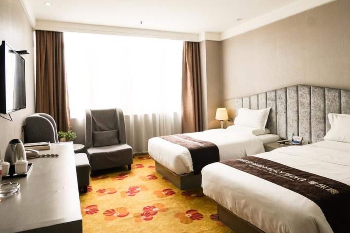 A hotel room with two beds, a desk, a chair, a TV, and a window with curtains.