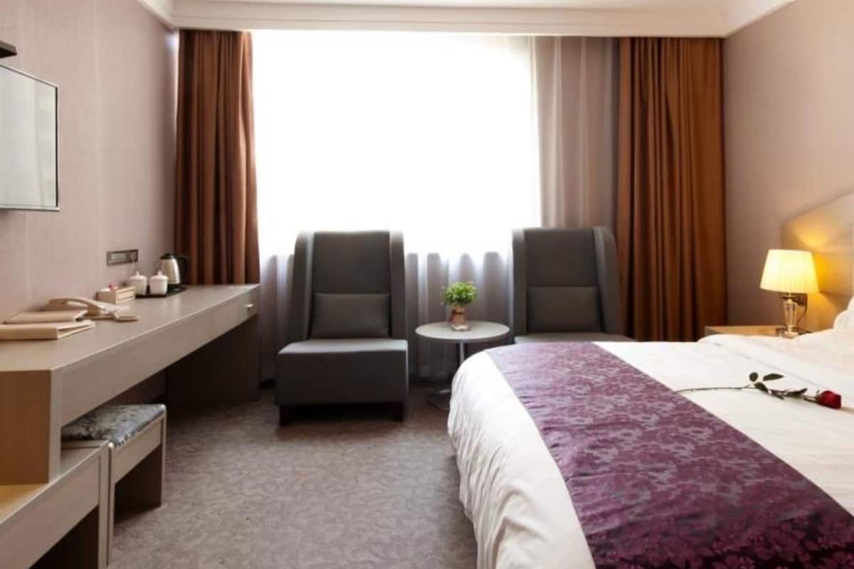 A hotel room with a bed, two armchairs, a desk, and a small table with a lamp.
