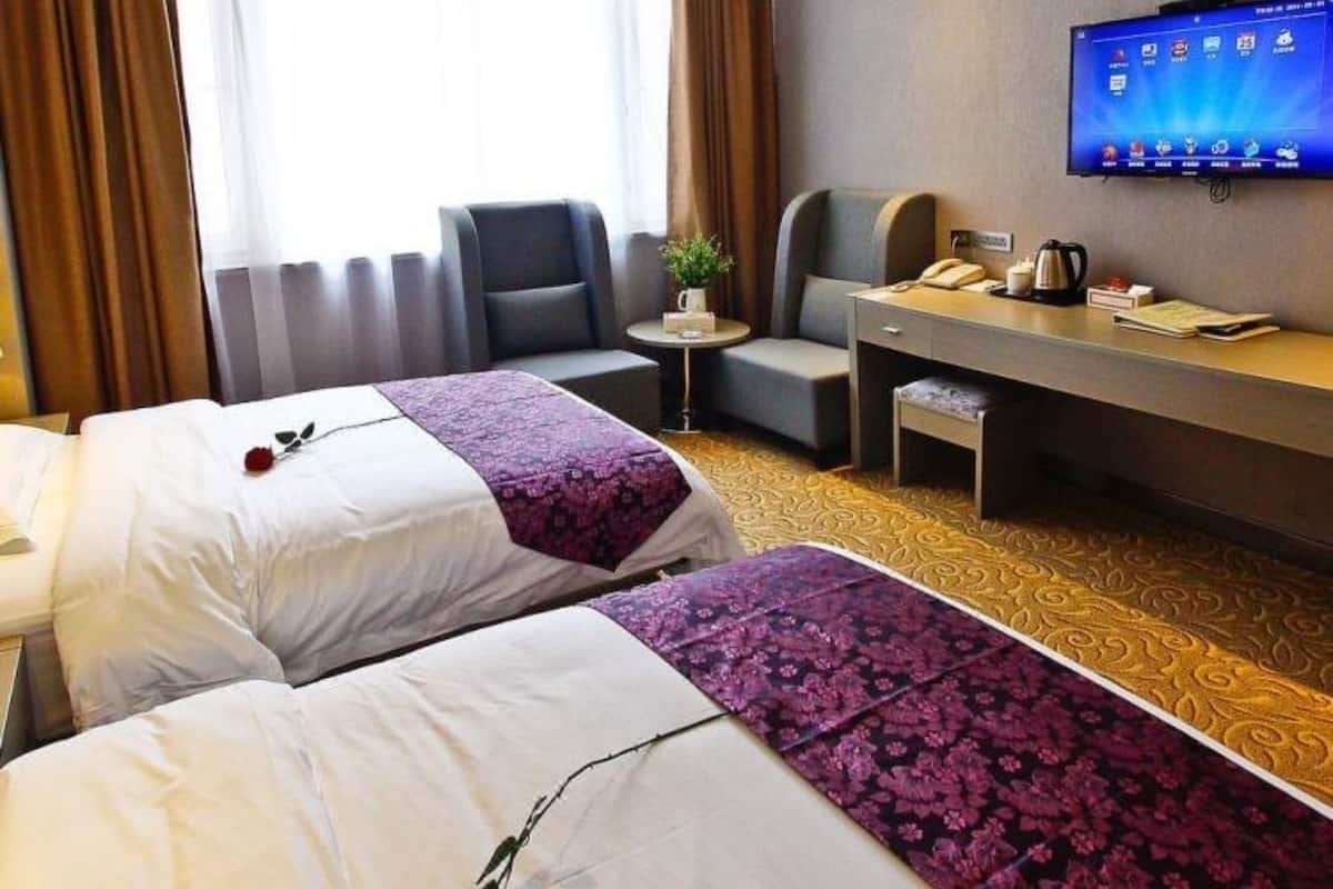 A hotel room with two beds, a desk, a chair, a television, and a window with curtains.