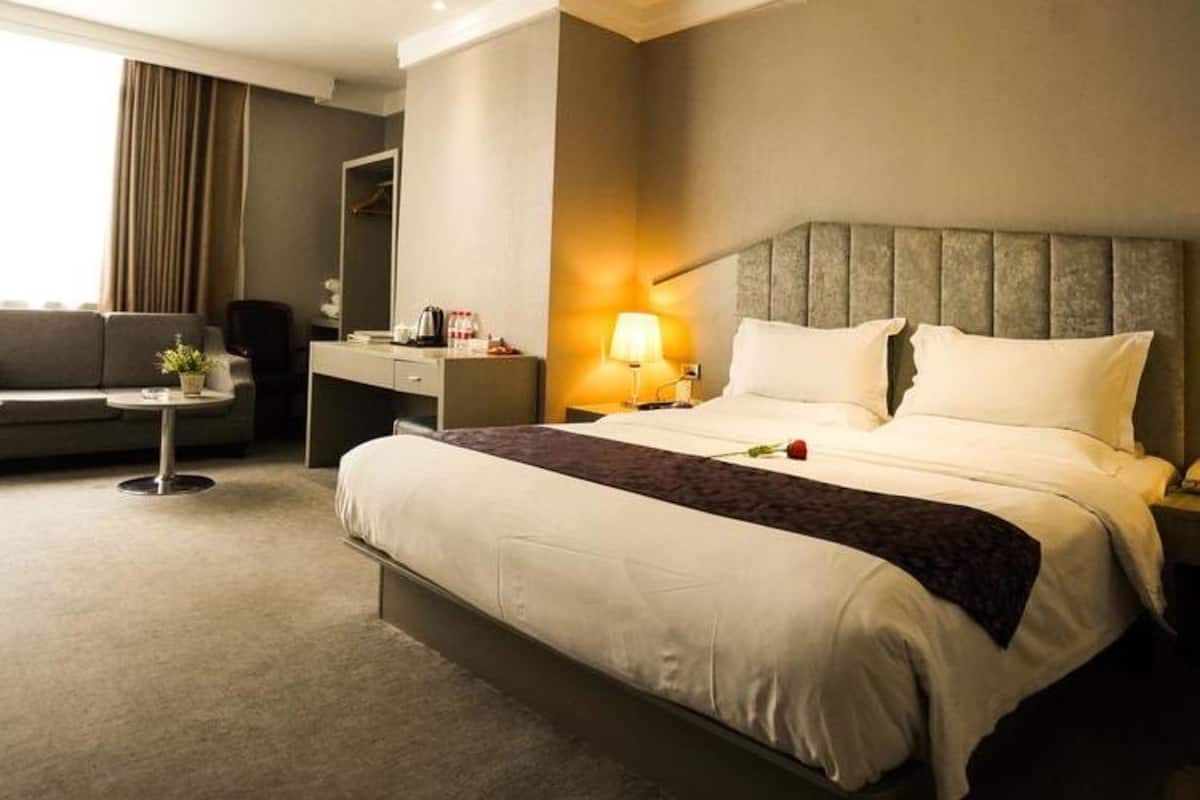 A hotel room with a large bed, bedside tables, a desk, a chair, and a window with curtains.