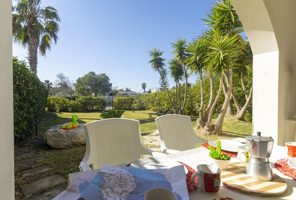 An outdoor dining area with white chairs, a table set with a map, a coffee pot, and a small plant.