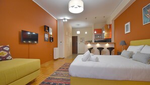 A hotel room with a bed, a sofa, a TV, and a kitchenette in the background. - Check Point - Down Town (Athens)