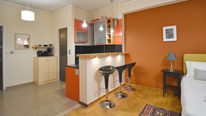 A compact hotel room with a kitchenette, a bed with a nightstand, and a small sitting area with a bar stool. - Check Point - Down Town (Athens)
