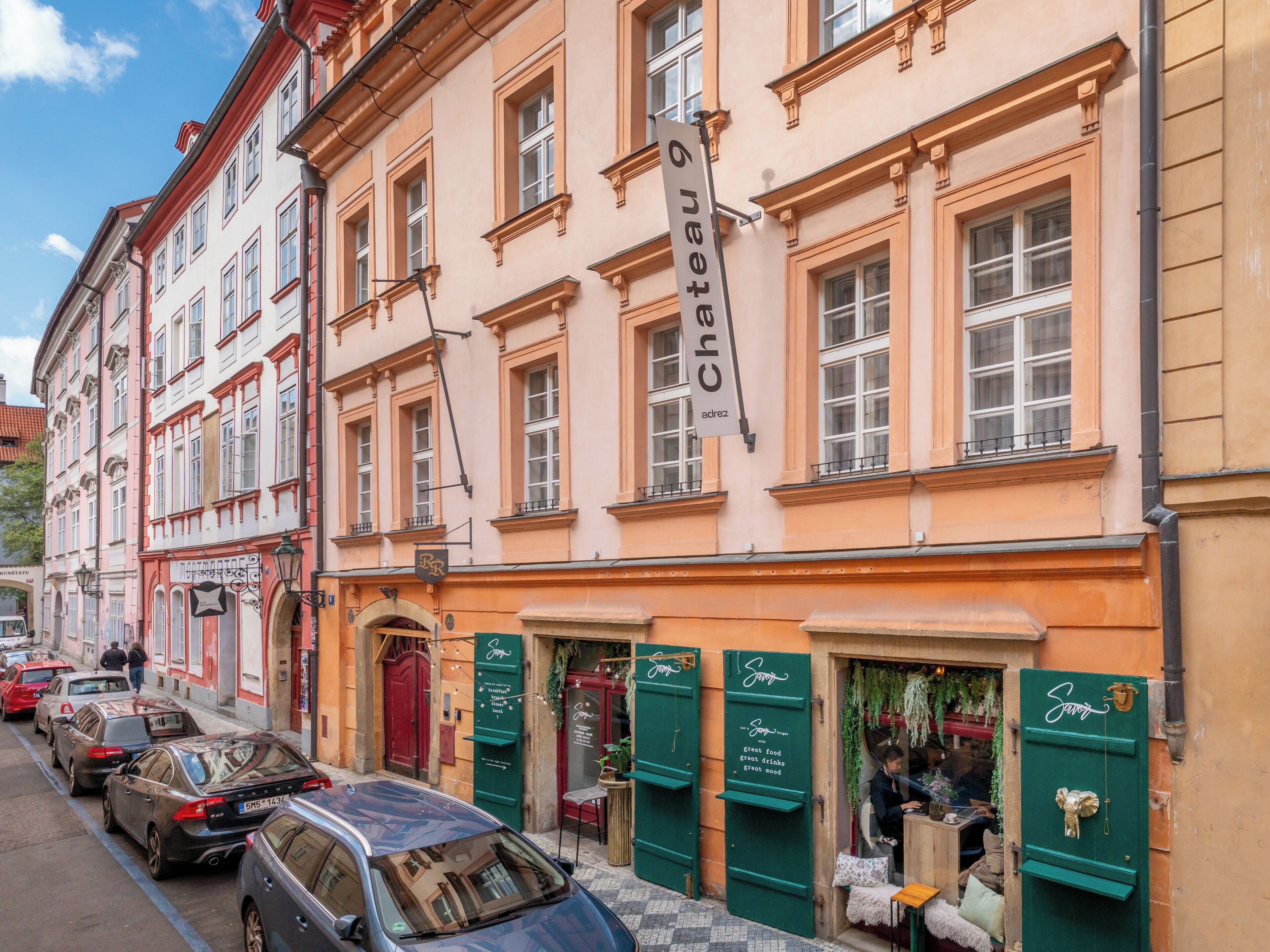 Une vue de rue avec des voitures garées, un bâtiment sur lequel on peut lire l’inscription « Château Adrez », et un magasin avec un auvent vert.