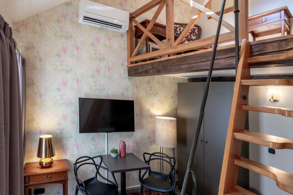 Habitación pequeña con literas, un televisor de pantalla plana, escritorio con lámpara, dos sillas y una alfombra estampada.