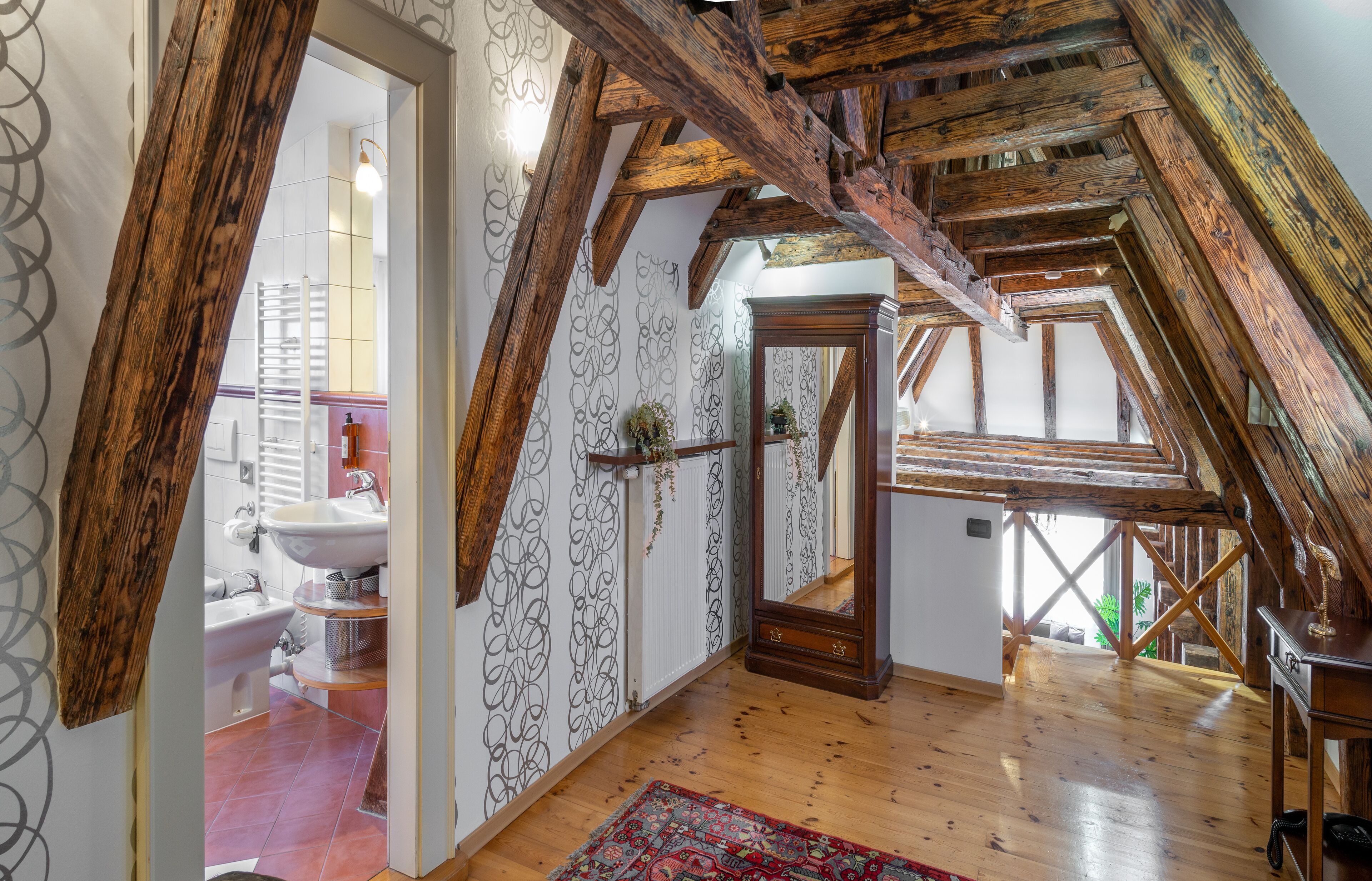 A rustic attic room with exposed wooden beams, a large mirror, and a view of the bathroom.