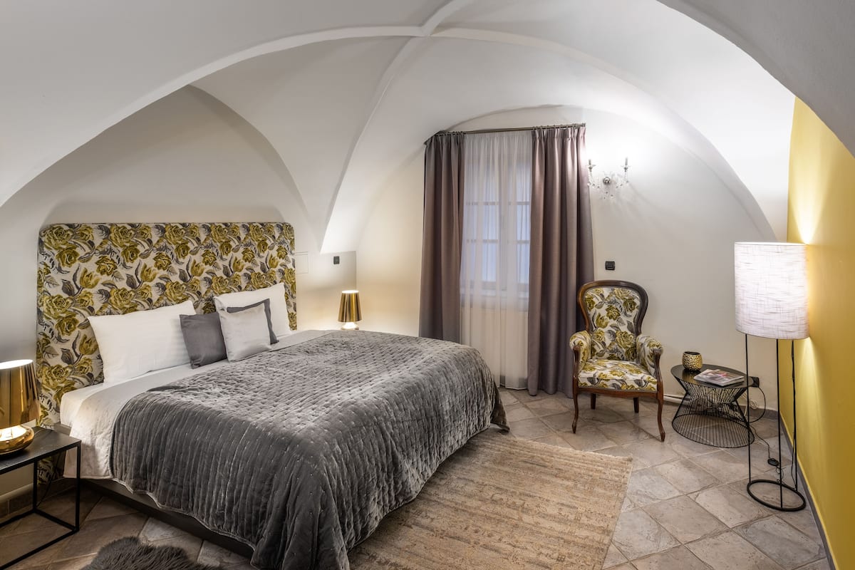 Un dormitorio con una cama grande, una silla, una lámpara y una mesita.