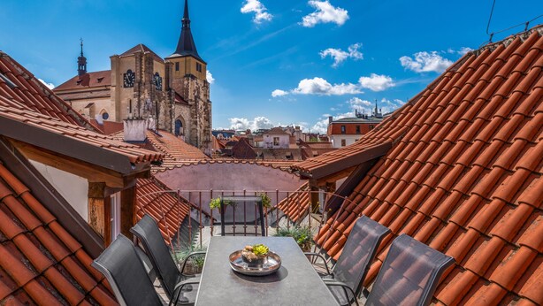 En tagterrasse med et bord og stole, udsigt til en kirke og terracotta tagsten.