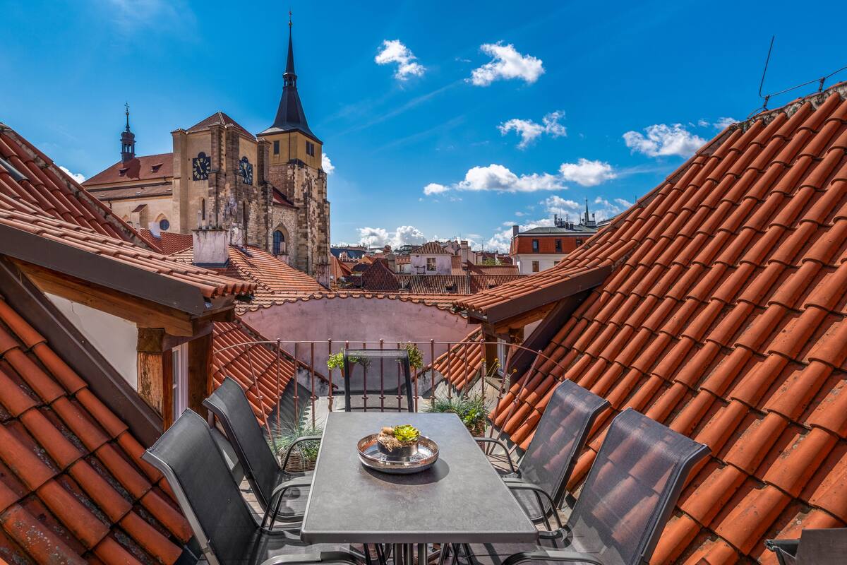 Terraza en la azotea con mesa y sillas, vista a una iglesia y tejas de barro.
