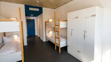 A dormitory room with bunk beds, a wardrobe, and a door.